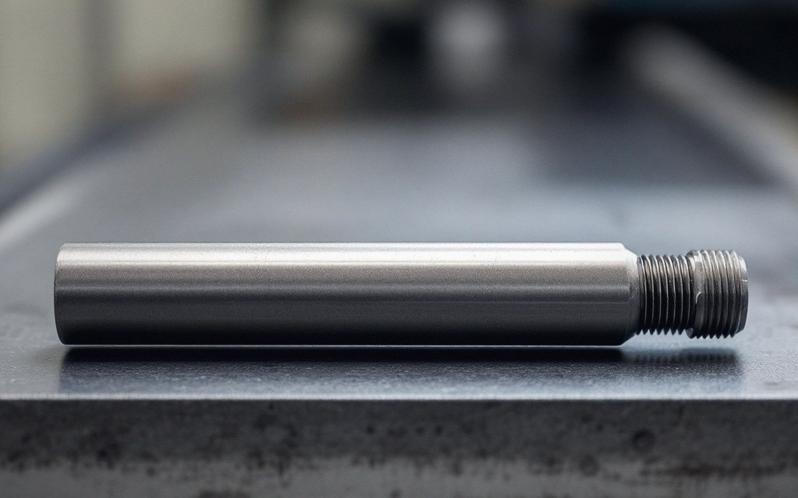 A machined metal rod with threaded end resting on a steel surface